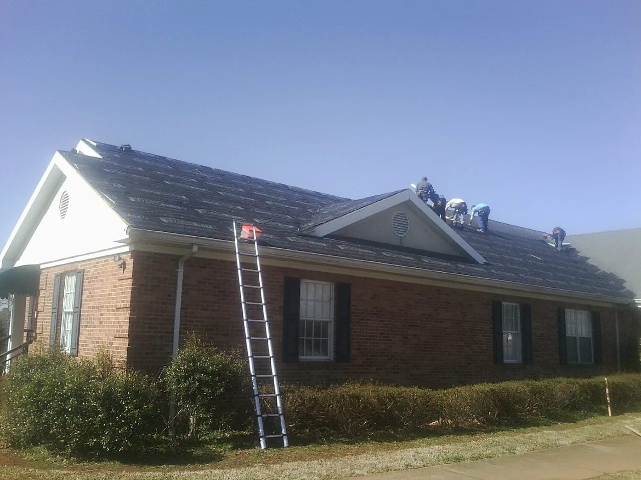 Crew tearing shingles off a brick ranch roof with a ladder set — Metal Roof Repair work by our crew in Cypress