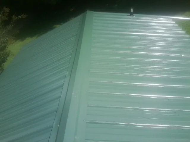 New green metal panels meeting at the ridge of a roof — Flat Roof Repair work by our crew in Cypress