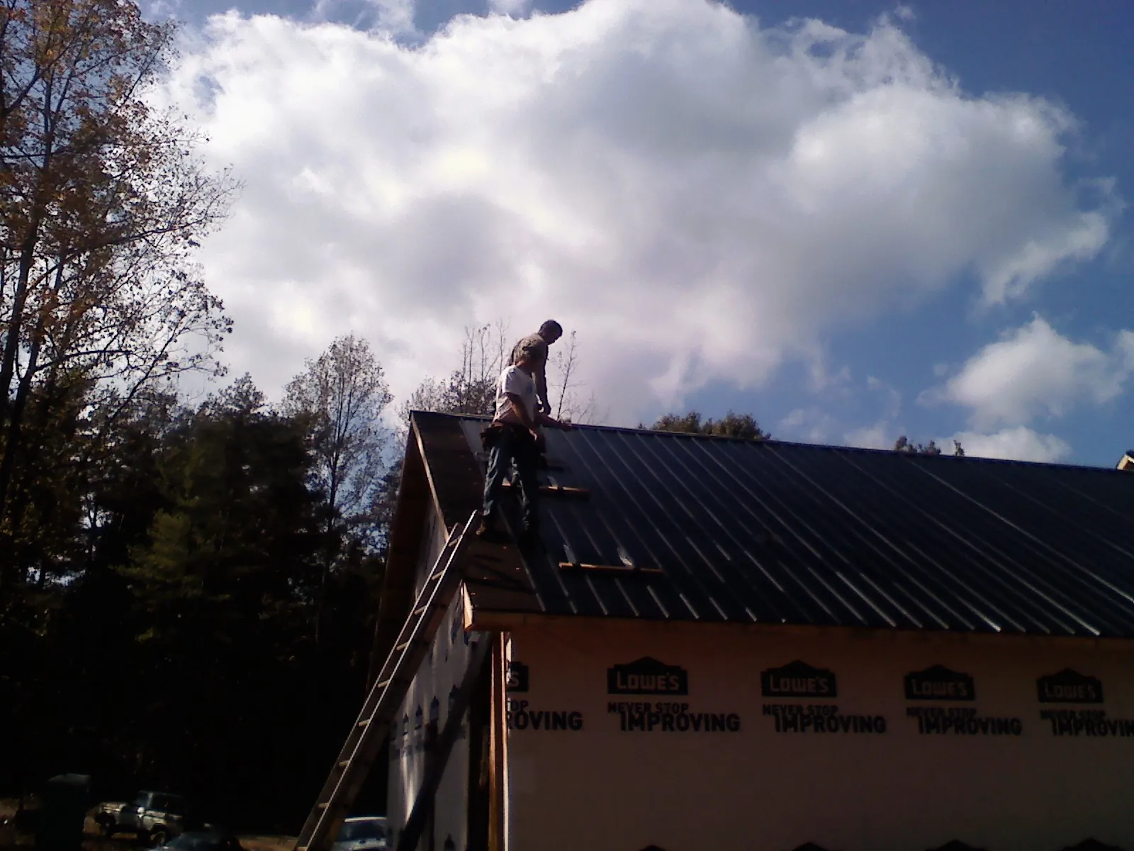 Roofer fastening dark metal panels high against a cloudy sky, from a Roof Inspection job in Cypress