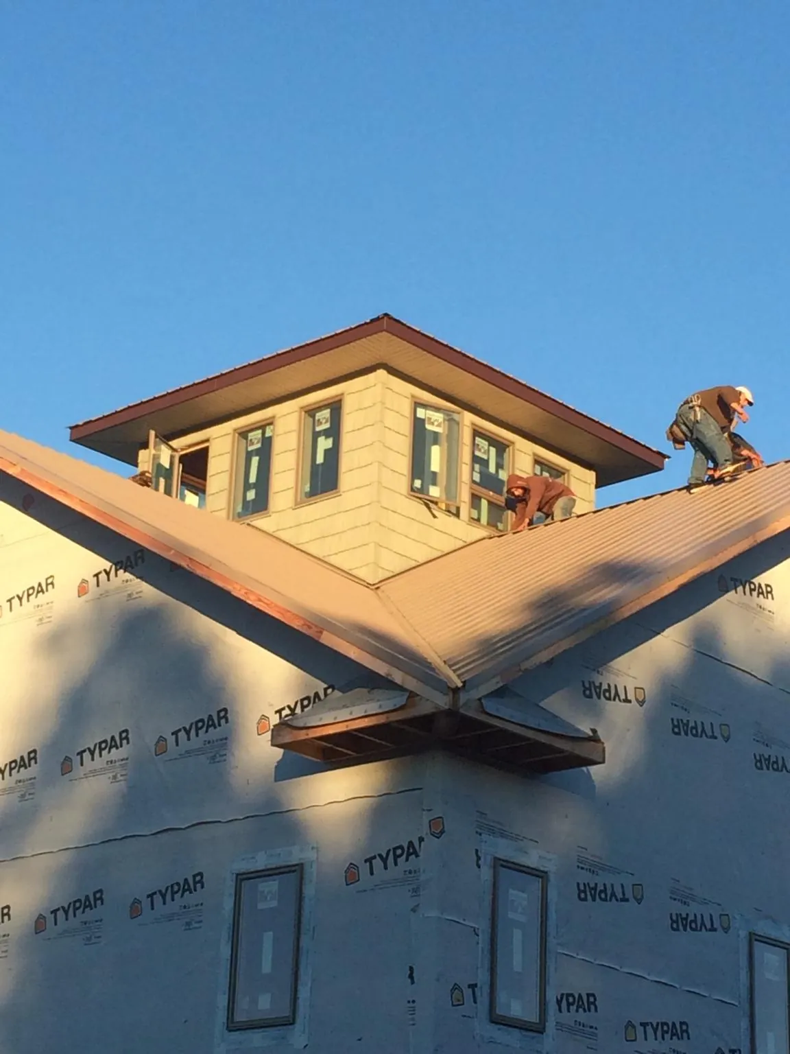 Roofers working around a rooftop cupola on a new metal roof at sunset — Roof Waterproofing in Cypress by Roofing Brothers